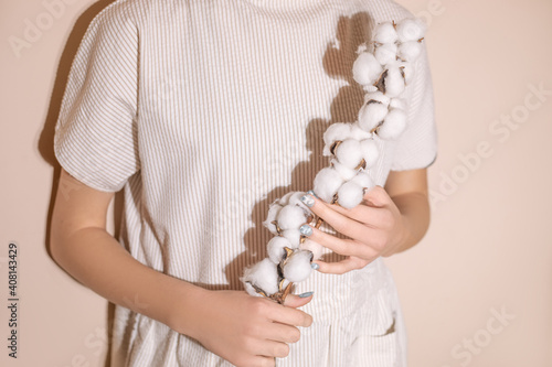 Photo of sprig of cotton with balls in female hands, dress made of natural materials. photo