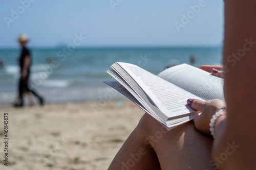 Woman reading a book on the beach  blurred background. Summer leisure on the beach