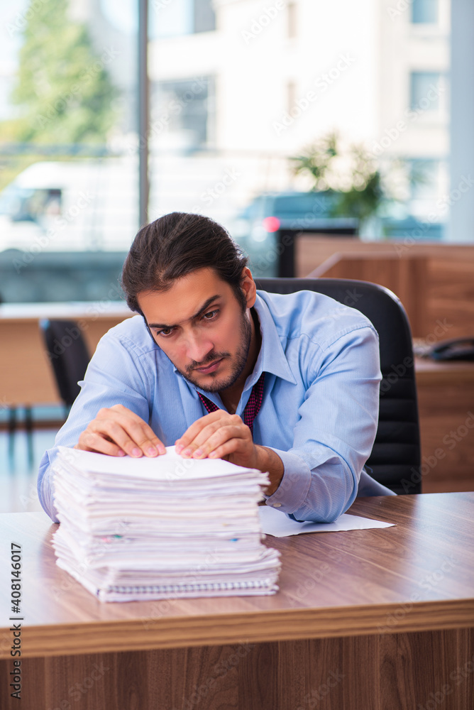 Young male employee unhappy with excessive work in the office Young male employee unhappy with excessive work in the office