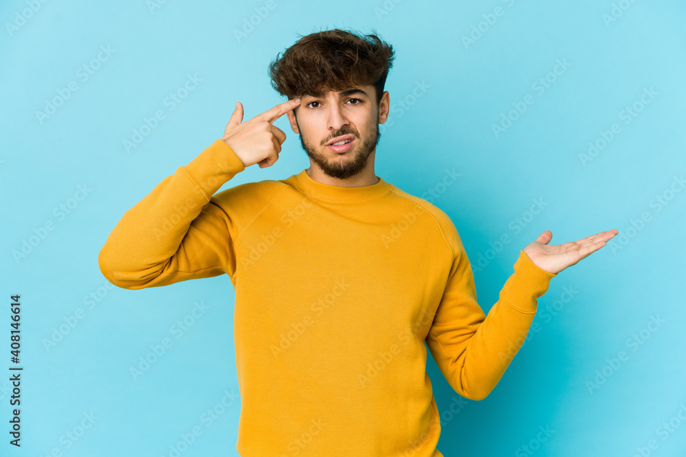 Young arab man on blue background holding and showing a product on hand. Young arab man on blue background holding and showing a product on hand.