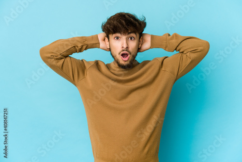 Young arab man on blue background screaming, very excited, passionate, satisfied with something.