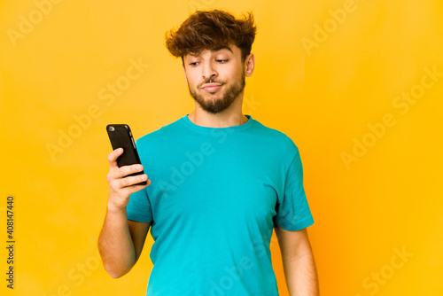 Young indian man holding a phone confused, feels doubtful and unsure.