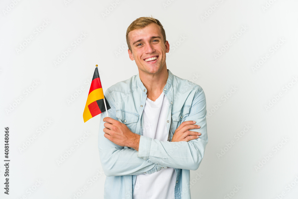 Young caucasian man holding a german flag isolated on white background - obrazy, fototapety, plakaty 