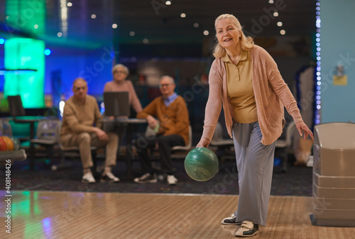 Fotografie Full length portrait of elegant senior woman playing bowling with group of frien