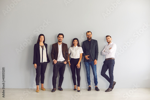 Team of happy young business people in smart casual office wear standing in studio and looking at camera. Group portrait of smiling company employees, startuppers or experienced business coaches