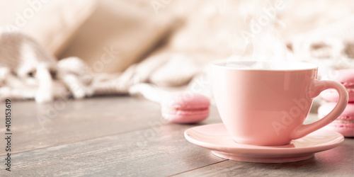 Cozy home composition. Book, plaid, steaming cup coffee or hot drink and macaroon on wooden table. Front view, copy space