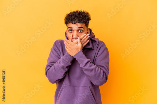 Young african american curly man isolated on purple shocked covering mouth with hands.