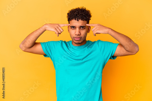 Young african american curly man isolated on purple focused on a task, keeping forefingers pointing head.