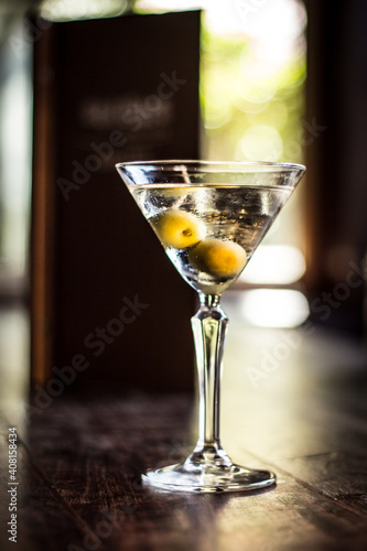 Martini cocktail alcohol drink beverage with olives and bokeh background on a wooden table