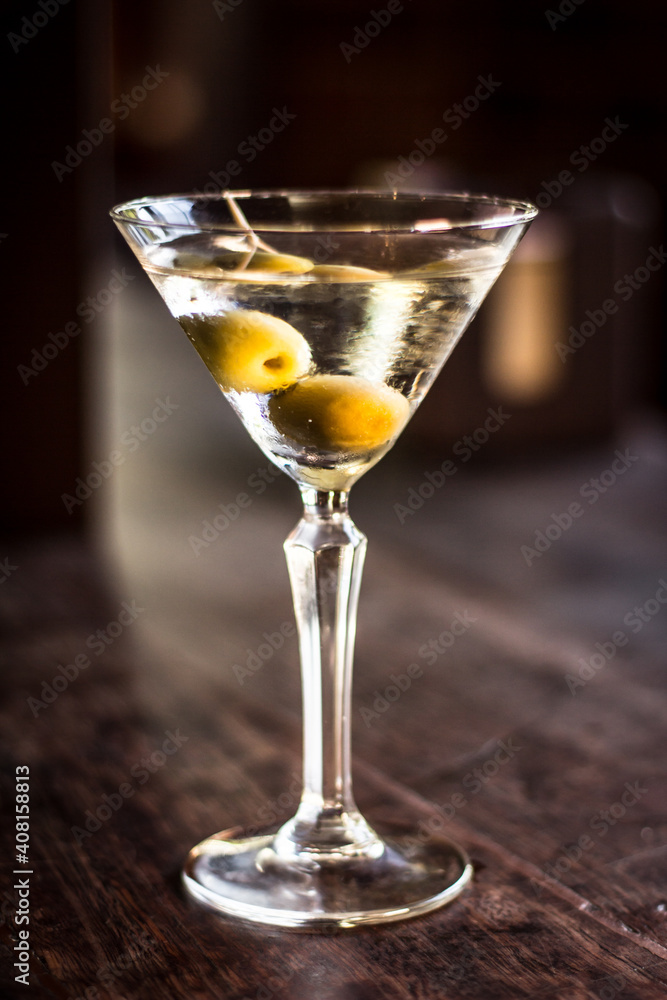 Martini cocktail alcohol drink beverage with olives and bokeh background on a wooden table