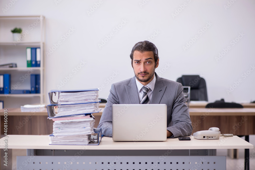 Young male employee unhappy with excessive work in the office Young male employee unhappy with excessive work in the office