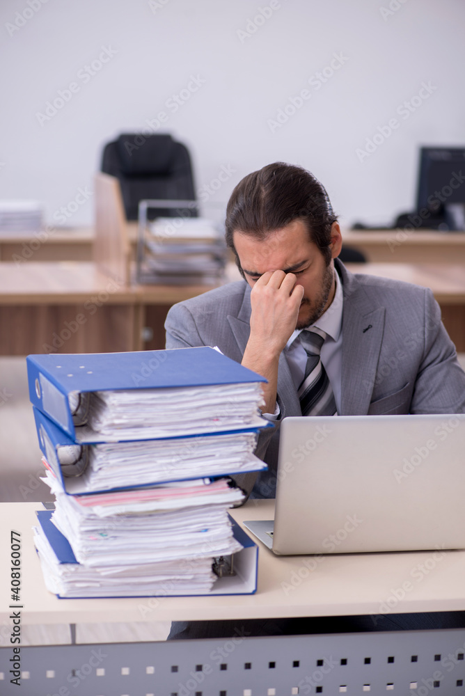 Young male employee unhappy with excessive work in the office Young male employee unhappy with excessive work in the office