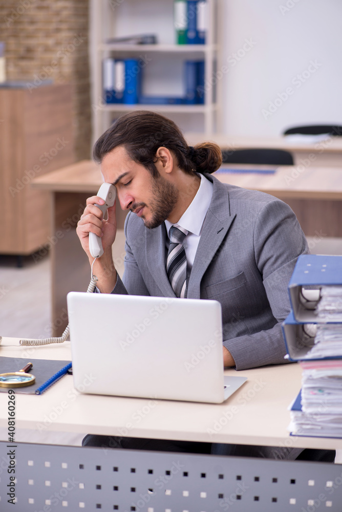 Young male employee unhappy with excessive work in the office Young male employee unhappy with excessive work in the office