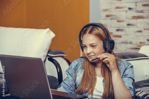 Happy teenage girl sitting on the floor wearing headphones, taking exam during a video call online with a laptop in the living room