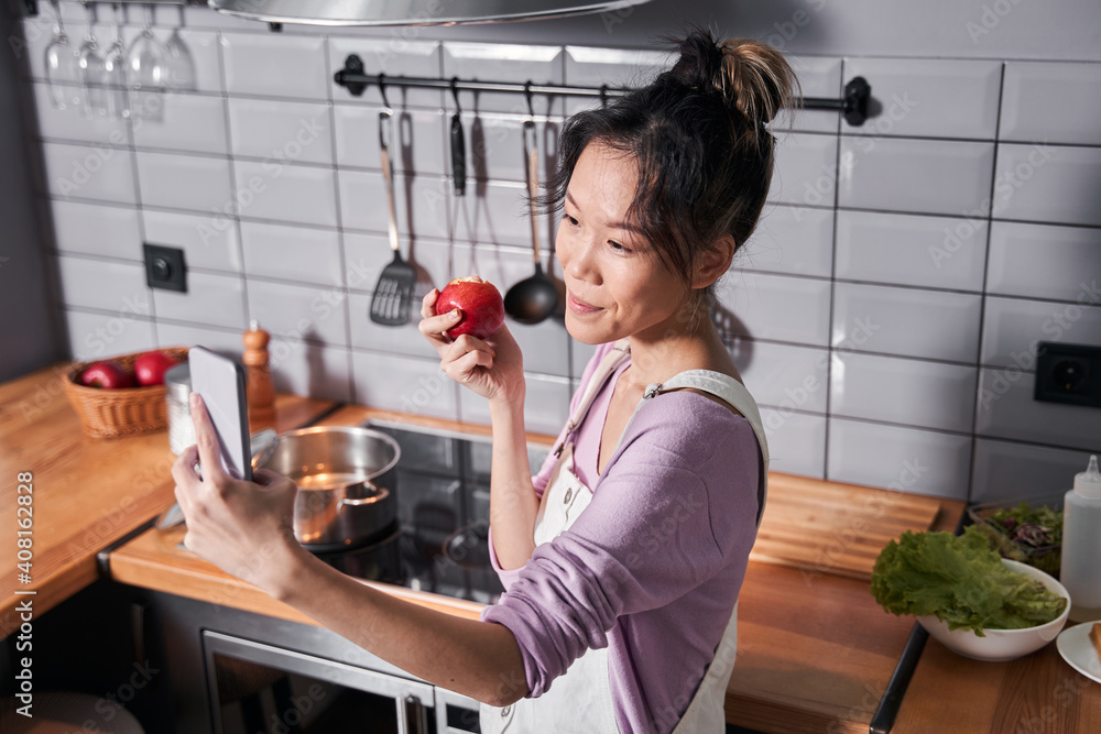 Woman making selfie while eating apple at kitchen