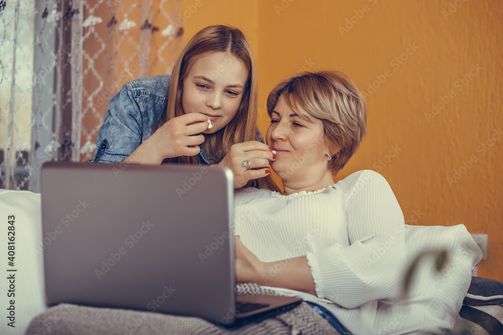 Mother and her teenage daughter are enjoy watching movies and eating popcorn while sitting on the couch Mother and her teenage daughter are enjoy watching movies and eating popcorn while sitting on the couch