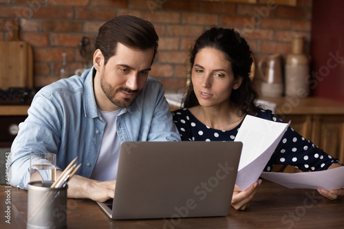 Young Caucasian couple look at laptop screen manage family financial paperwork paying bills online. Millennial man and woman work on computer, use web banking system for payment on gadget.
