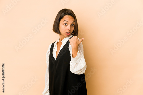 Young hispanic woman isolated points with thumb finger away, laughing and carefree.