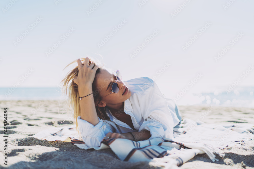 Portrait of a beautiful Caucasian woman touching her hair and looking aside while enjoying a spare time at the beachside. Blonde hipster girl in modern sunglasses and trendy outfit relaxing at seaside Portrait of a beautiful Caucasian woman touching her hair and looking aside while enjoying a spare time at the beachside. Blonde hipster girl in modern sunglasses and trendy outfit relaxing at seaside