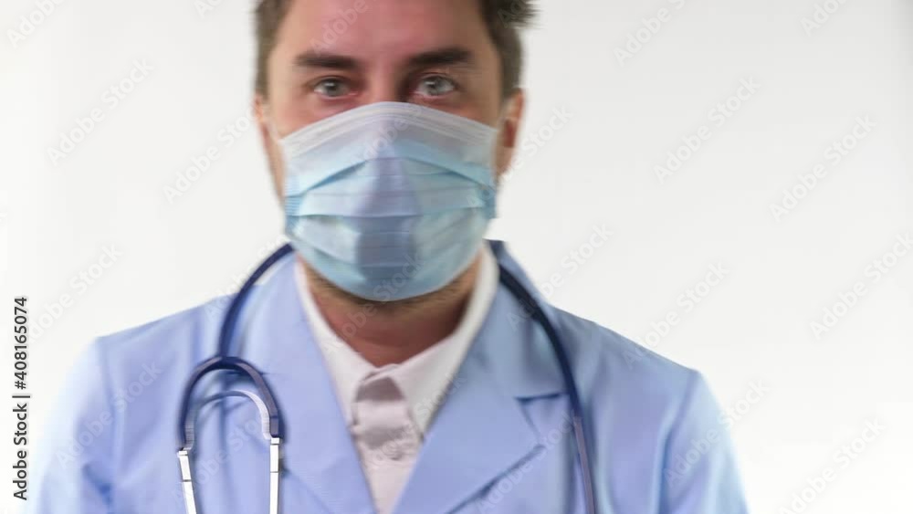 Young doctor stand and hold stethoscope in hand in blue gloves. Man in blue medical uniform on white background Young doctor stand and hold stethoscope in hand in blue gloves. Man in blue medical uniform on white background