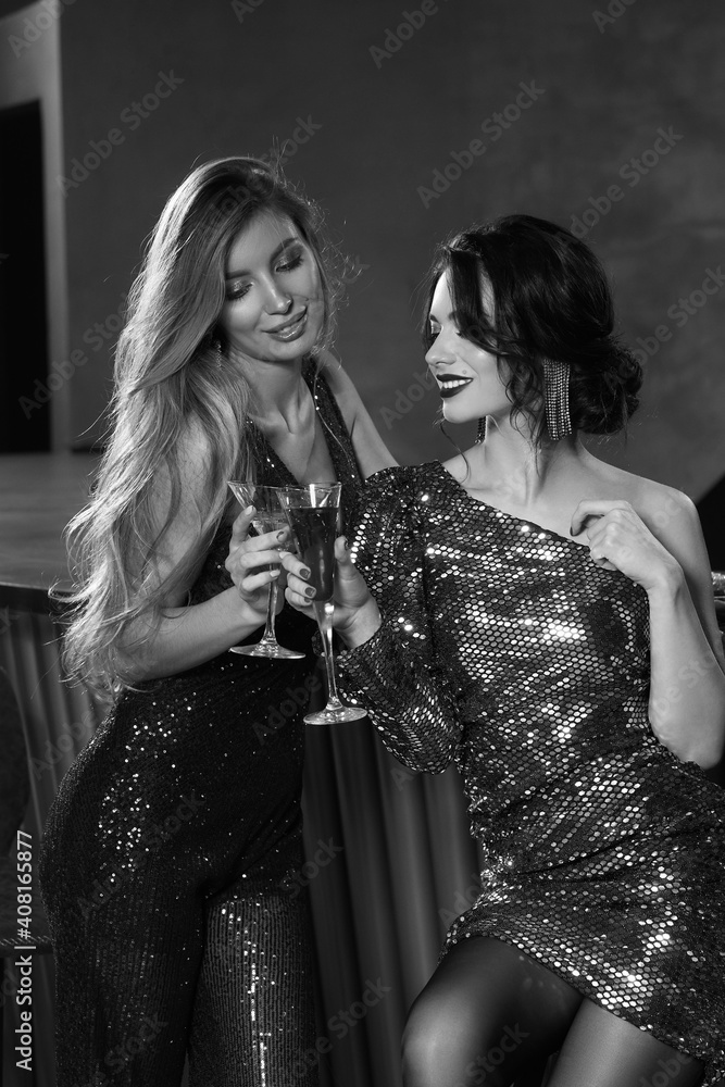 Two girls having fun in bar. Elegant woman in fahionable sequins dresses. Nightclub party. Female celebrating, having fun in bar. Beautiful caucasian blonde and brunette ladies Two girls having fun in bar. Elegant woman in fahionable sequins dresses. Nightclub party. Female celebrating, having fun in bar. Beautiful caucasian blonde and brunette ladies