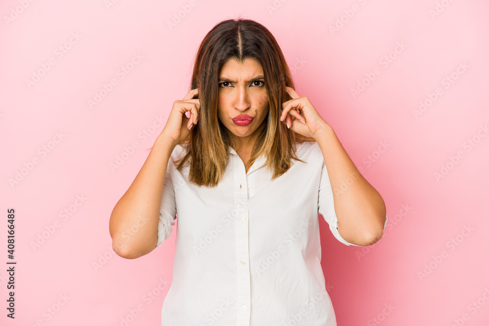 Young indian woman isolated on pink background covering ears with fingers, stressed and desperate by a loudly ambient. Young indian woman isolated on pink background covering ears with fingers, stressed and desperate by a loudly ambient.