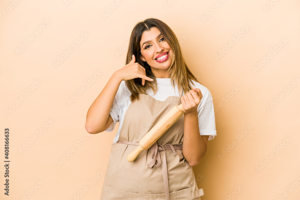 Young indian pastry chef woman isolated showing a mobile phone call gesture with fingers. Young indian pastry chef woman isolated showing a mobile phone call gesture with fingers.