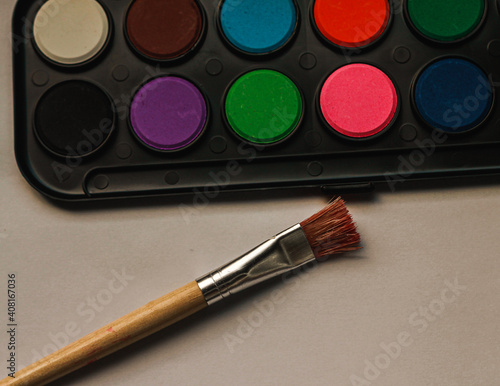 Closeup shot of colorful paints on a box and a brushon the beige background photo