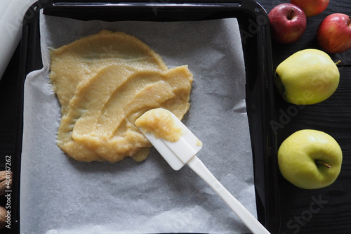 Top view of making roll-up pastila,homemade fruit leather . Fruit puree on a black baking sheet with a white spatula on a wooden table. The concept of making natural sweets from apples and bananas