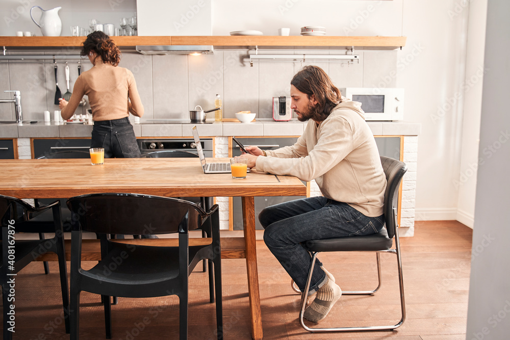 Man working at the laptop while his wife preparing breakfast