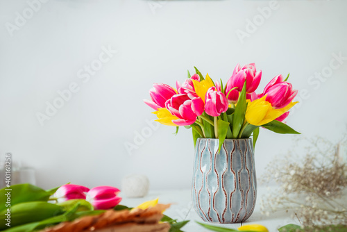 Fresh spring yellow and pink tulips bouquet in a vase, other flowers and details on florist workspace on white wooden table. Education of floristry. Selective focus. Copy space.