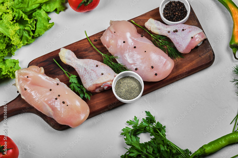 Wooden plate of raw chicken fillet and legs with spices and vegetables on white table Wooden plate of raw chicken fillet and legs with spices and vegetables on white table