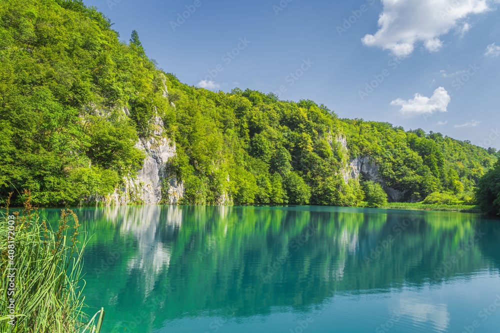 Panoramic view with tall cliff covered in trees and turquoise coloured lake underneath it. Plitvice Lakes National Park UNESCO World Heritage, Croatia