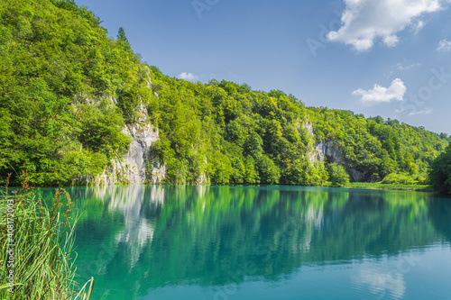 Panoramic view with tall cliff covered in trees and turquoise coloured lake underneath it. Plitvice Lakes National Park UNESCO World Heritage  Croatia