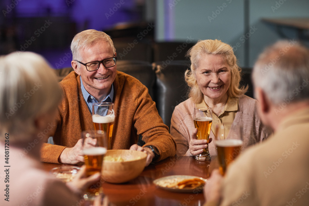 Group of smiling senior people drinking beer in bar while enjoying night out with friends, copy space