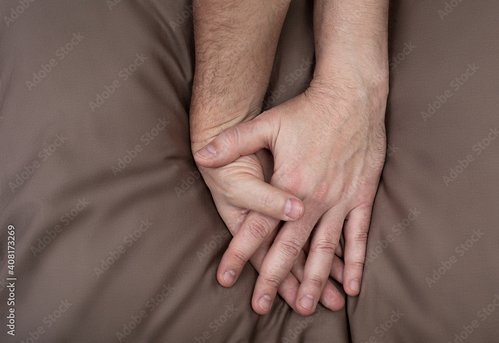 Fototapeta premium LGBT concept. Men holding hands on the bed. Hands of couple of homosexual men on brown pillow. Same sex love. Gay relationships.