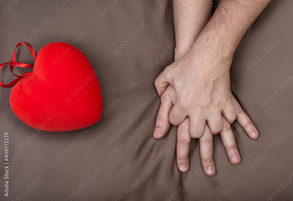 LGBT concept. Men holding hands with passion on the bed near red heart. Hands of couple of homosexual men on brown pillow. Same sex love. Gay relationships. Valentines card for gays LGBT concept. Men holding hands with passion on the bed near red heart. Hands of couple of homosexual men on brown pillow. Same sex love. Gay relationships. Valentines card for gays