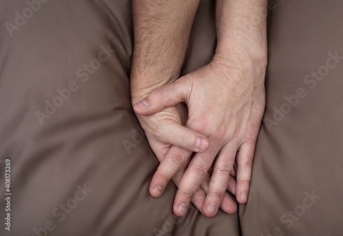 LGBT concept. Men holding hands on the bed. Hands of couple of homosexual men on brown pillow. Same sex love. Gay relationships.