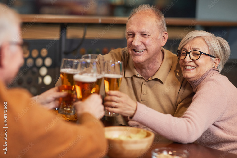 Portrait of smiling senior couple drinking beer in bar and clinking glasses while enjoying night out with friends Portrait of smiling senior couple drinking beer in bar and clinking glasses while enjoying night out with friends