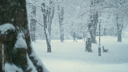 CLOSE UP: Blurry person in distance walks in the quiet park during a blizzard.