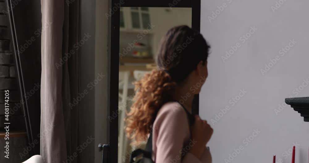 Smiling millennial attractive caucasian woman looking in mirror, standing in hallway with backpack on shoulders, checking neat casual look before going outside for walk, dating or meeting with friends Smiling millennial attractive caucasian woman looking in mirror, standing in hallway with backpack on shoulders, checking neat casual look before going outside for walk, dating or meeting with friends