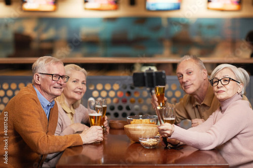 Group of modern senior people taking selfie photo while drinking beer in bowling bar and enjoying night out with friends, copy space
