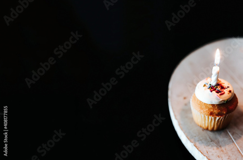 first birthday cupcake with sprinkles and one candle on rustic farmhouse platter and black background 