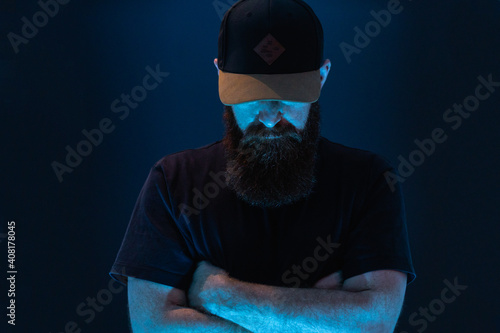 man with beard and baseball cap with dark and blue background unrecognizable face 
