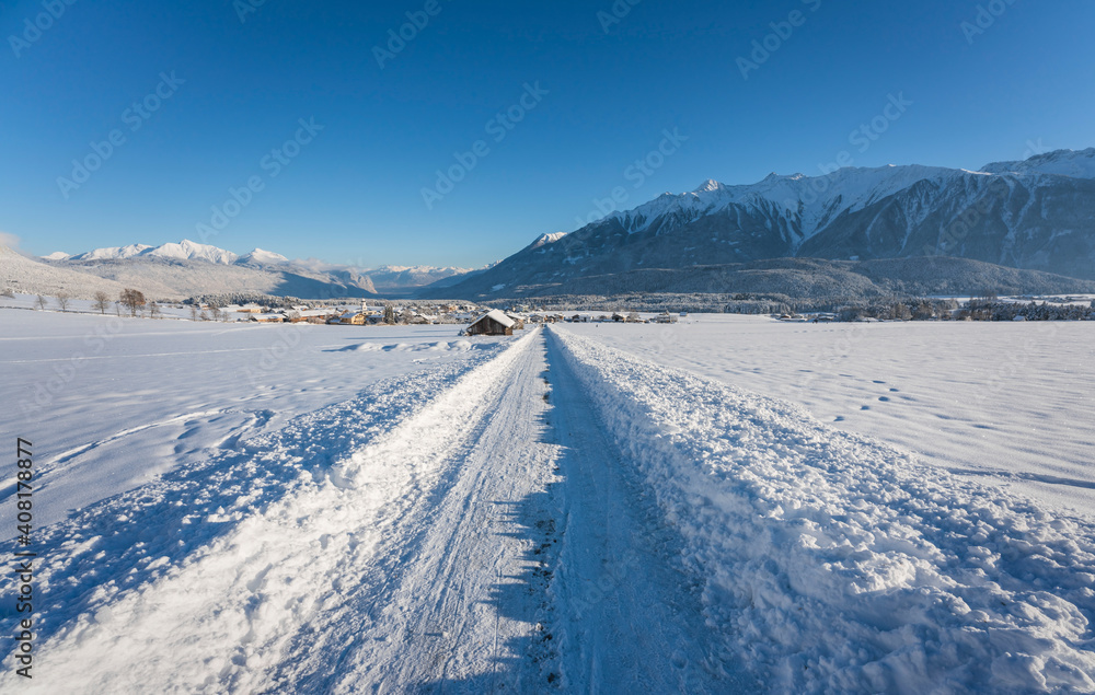 Snow covered walking path through alpine winter landscape to the village of Wildermieming, Tirol, Austria