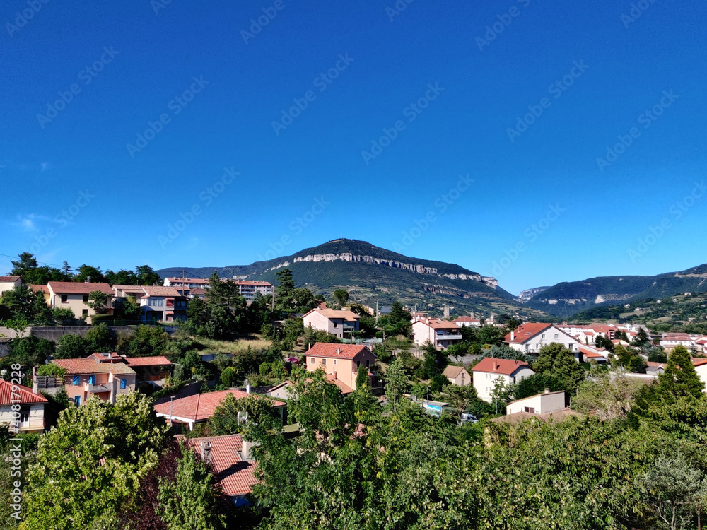 A panoramic view of a small old French village surrounded by nature during a summer day over a blue cloudy sky. Aveyron, France.