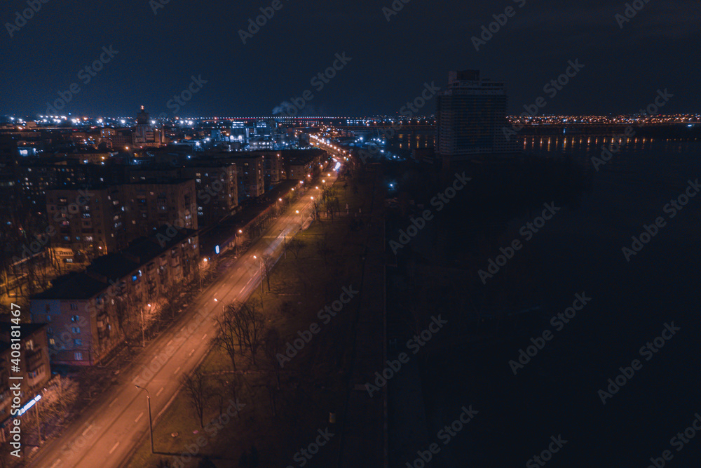 Fototapeta premium Drone view at night, with illuminated streets and dark sky. Beautiful cityscape