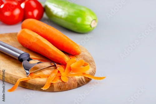 Peeling raw vegetables at wooden chopping board on grey surface with copy space. Healthy food concept. © Sergey