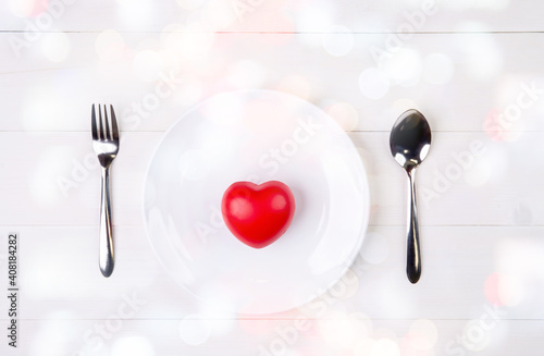Valentine day, heart shape on dish and utensil with bow for dinner on wooden table, spoon and fork and plate on desk, anniversary and celebration of love, copy space, top view, holiday concept.