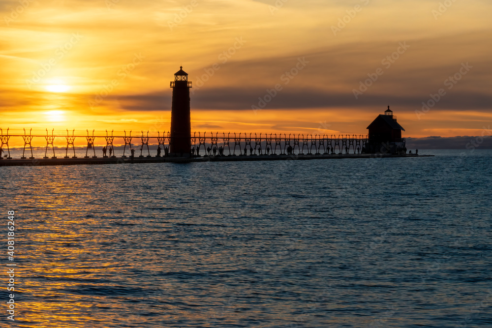 Grand Haven Lighthouse Michigan on Lake Michigan at sunset during the winter with beautiful colors and the structures and people silhouetted.  Hot from North Pier.